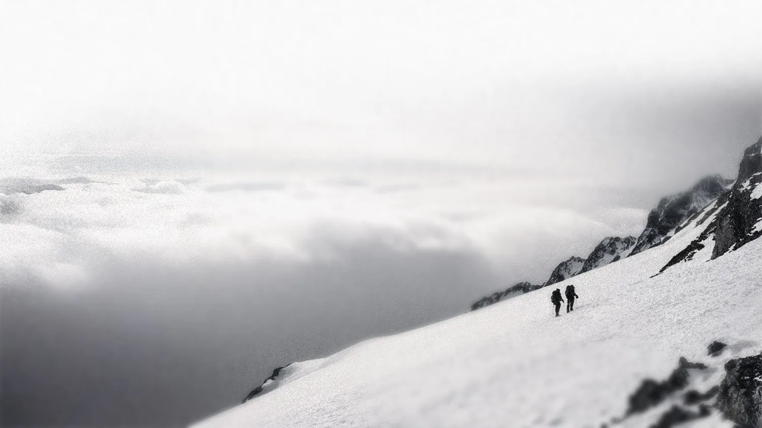 Two climbers crossing a snowy ridge above the clouds